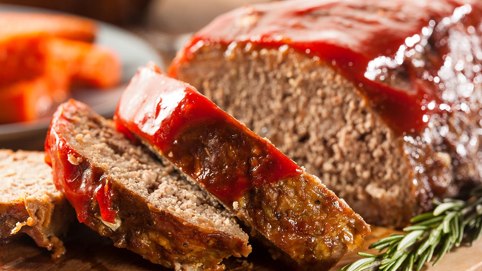 Slices of meatloaf covered in red sauce on a cutting board