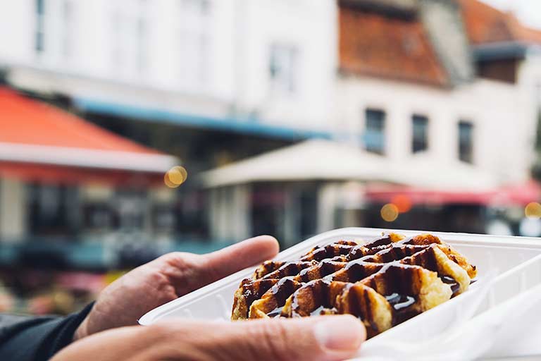 A person holding a Belgian waffle covered in chocolate