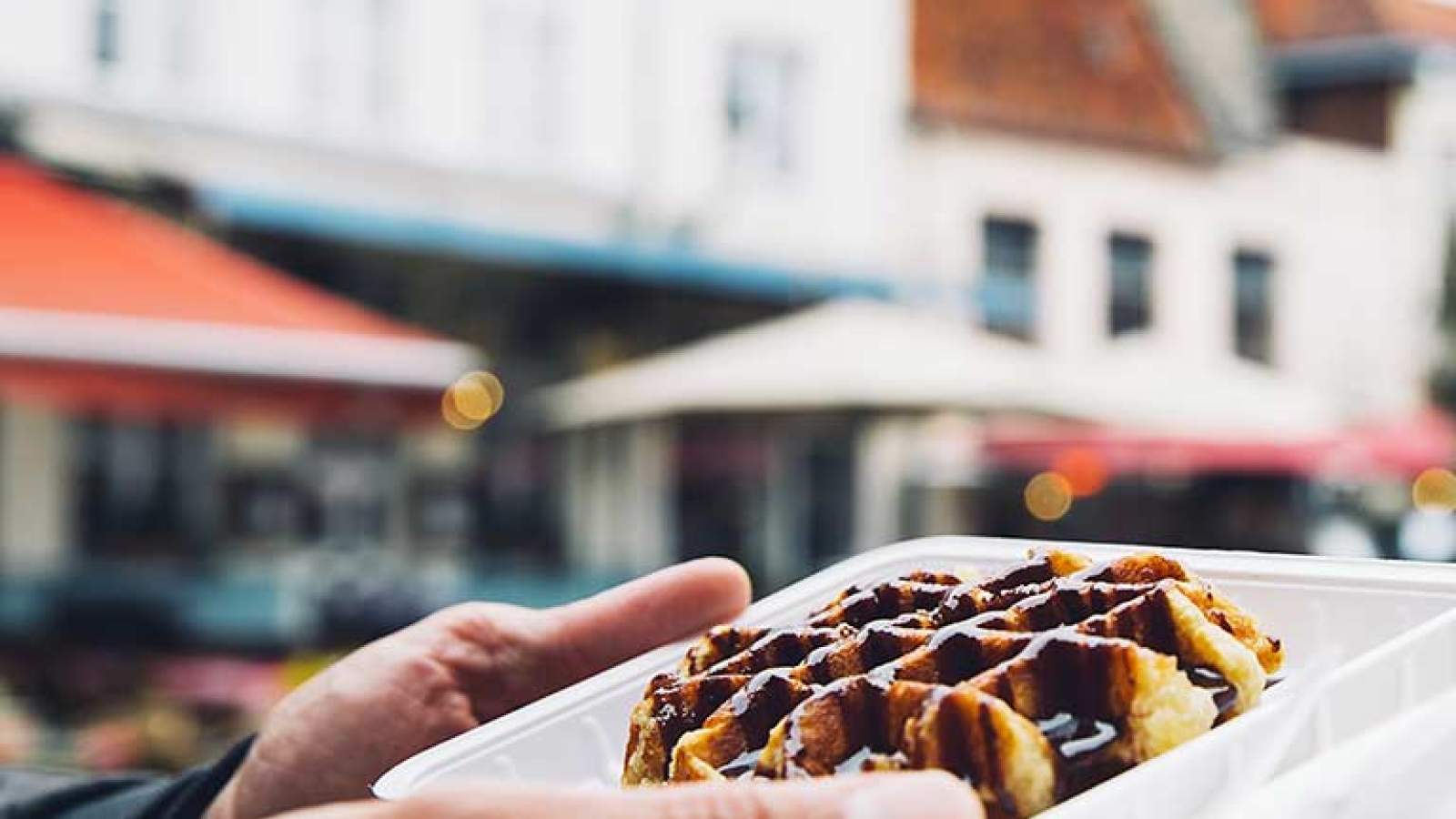 A person holding a Belgian waffle covered in chocolate